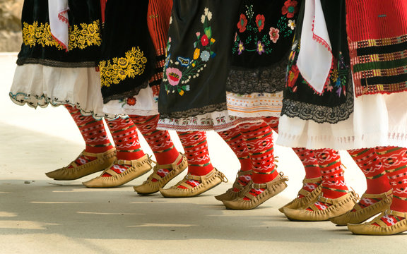Girls dancing folk dance. People in traditional costumes dance Bulgarian folk dances. Close-up of female legs with traditional shoes, socks and costumes for folk dances.