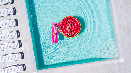 Aerial view of two women floating on inflatable mattresses relaxing in the swimming pool. Summer...