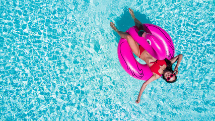 Young pretty woman in in a colorful bikini, lies on a pink flamingo floating in pool. Summer vocation.