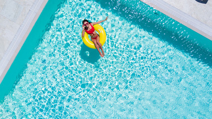 Aerial view of young sexy woman in bikini swimming on the inflatable big yellow ring in pool