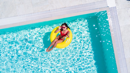 Aerial view of young sexy woman in bikini swimming on the inflatable big yellow ring in pool