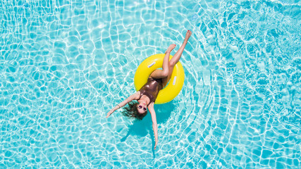 Aerial view of young sexy woman in bikini swimming on the inflatable big yellow ring in pool