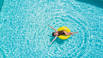 Vacation concept. Top view of slim young woman in bikini on the yellow air inflatable ring in the swimming pool.