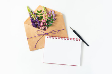 Festive composition: on a white table lies an envelope, notebook, fountain pen and flowers. Concept of Mother's Day and International Women's Day. View from above.Tropical flowers on light litter