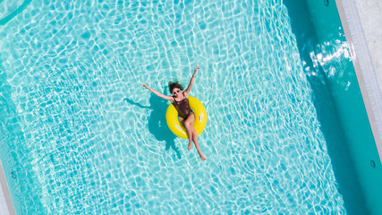 Happy young woman in bikini with rubber inflatable float, playing and having a good time at water fun park pool, on a summer hot day