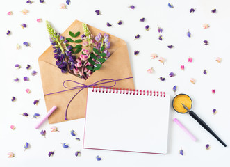 Festive composition: on a white table lies an envelope, notebook, fountain pen and flowers. Concept of Mother's Day and International Women's Day. View from above.Tropical flowers on light litter