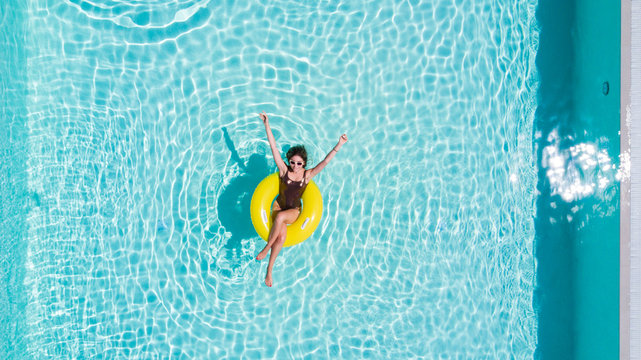 Vacation concept. Top view of slim young woman in bikini on the yellow air inflatable ring in the swimming pool.