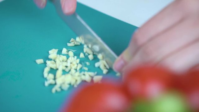 Female hands cutting garlic on a cutting board with red pepper on the foreground