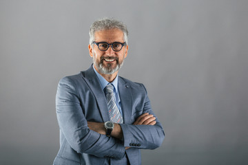 senior businessman posing crossed arms on gray background