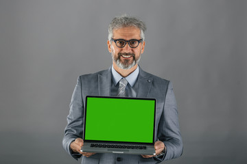senior businessman holding laptop with green screen on gray background