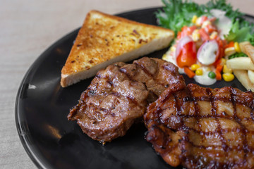 The roasted pork with buttered bread and french fried and vegetable in the dark plate in the natural light. 