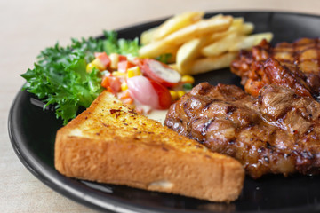 The roasted pork with buttered bread and french fried and vegetable in the dark plate in the natural light. 