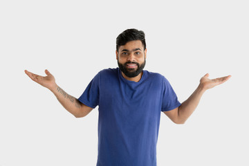 Fototapeta premium Beautiful male half-length portrait isolated on white studio background. Young emotional hindu man in blue shirt. Facial expression, human emotions, advertising concept. Presenting and inviting.