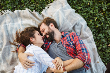 Image of young couple man and woman hugging and looking at each other while lying in green park