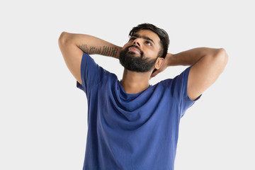 Beautiful male half-length portrait isolated on white studio background. Young emotional hindu man in blue shirt. Facial expression, human emotions, advertising concept. Standing and resting, dreaming