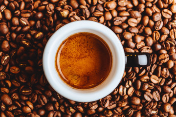 Roasted coffee beans with cup of espresso on dark background