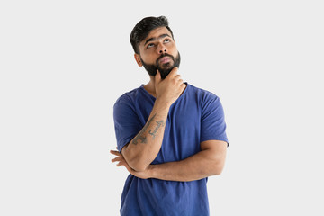 Beautiful male half-length portrait isolated on white studio background. Young emotional hindu man in blue shirt. Facial expression, human emotions, advertising concept. Thinking or choosing.