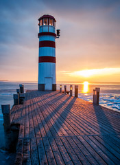 Winter landscape with lighthouse on a lake at sunset