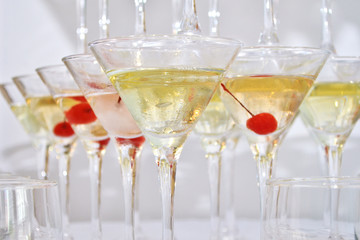 Triangular martini glasses, filled with champagne with cherries built in the shape of a pyramid, closeup