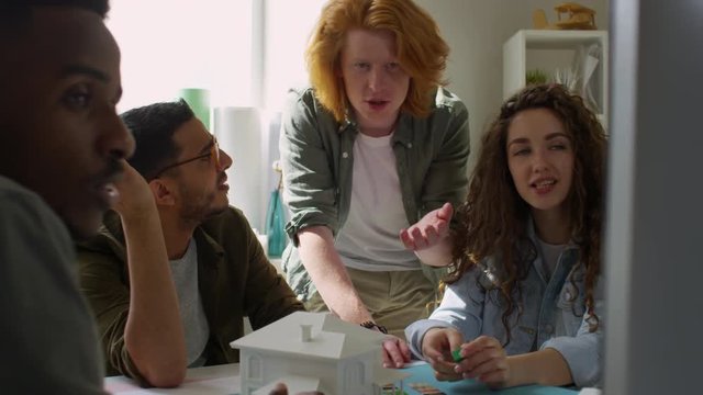 Tilting medium shot of cheerful young multi-ethnic creative team having animated discussion while looking at computer screen, gesturing, smiling and laughing