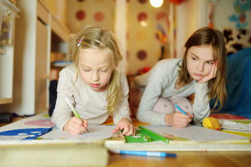 Two cute little sisters writing letters together at home. Older sister helping youngster with her homework.