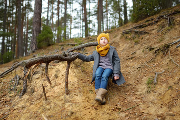 Naklejka premium Adorable young girl having fun on beautiful autumn day. Happy child playing in autumn park. Kid exploring fall forest.