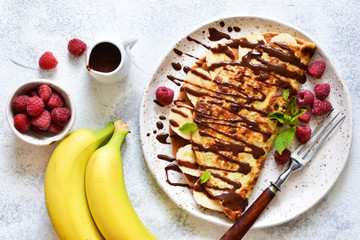 Crepe with chocolate paste, banana and raspberries on a concrete background. Tasty breakfast.