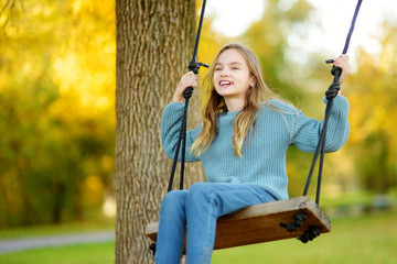Cute young girl having fun on a swing in sunny autumn park. Family weekend in a city.