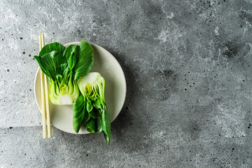 Baby bok choi halves on a plate gray background. Top view, horizontal orientation with copy space - obrazy, fototapety, plakaty