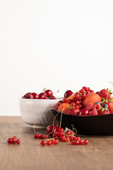 selective focus of red cherries in white bowl and mixed berries on plate on wooden table isolated on white