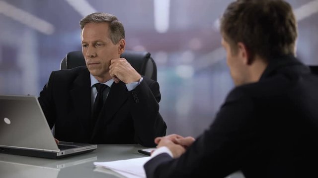 Inattentive man hirer looking at laptop during job interview with male candidate