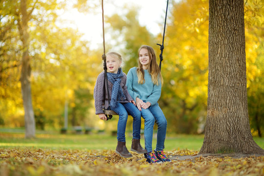 Cute young girl having fun on a swing in sunny autumn park. Family weekend in a city.