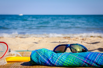 Snorkel, sunglasses and blue plaid dress are placed on mat at the sandy beach.