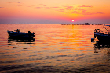 Naklejka na ściany i meble Silhouetted shot of beautiful sunrise with fisherman boat on the water