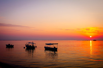 Fototapeta na wymiar Silhouetted shot of beautiful sunrise with fisherman boats on the water