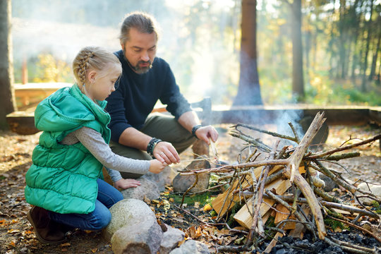 Cute young girl learning to start a bonfire. Father teaching her daughter to make a fire. Child having fun at camp fire. Camping with kids in fall forest.