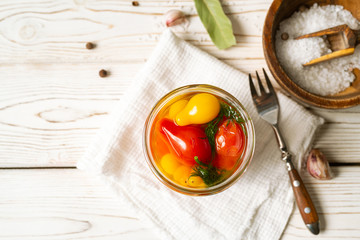 Marinated tomatoes in open glass jar, fork, cooking ingredients on white background. Horizontal image, top view.