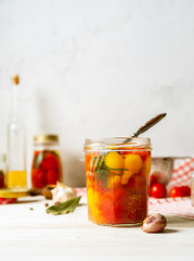 Marinated tomatoes in open glass jar, assorted vegetable preserves on white background. Vertical image.