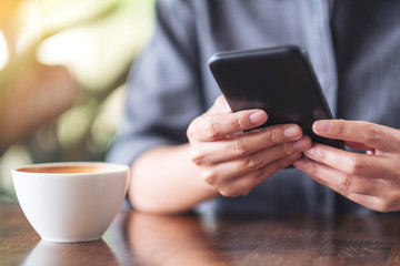 Closeup image of a woman holding  and using mobile phone with coffee cup on wooden table in cafe