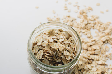 Jar and scatterd raw oat-flakes on white background