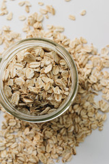 Jar and scatterd raw oat-flakes on white background