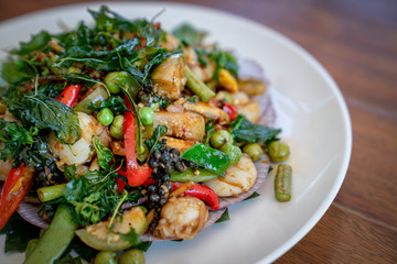 a Thai food Seafood fried in a spicy sauce in white circle dish on wooden table background.