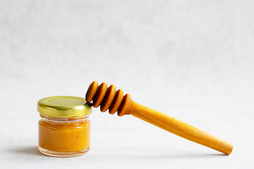 Small glass jar with metal cap with light yellow honey and special wooden spoon isolate on grey cement background with copy space. Healthy product, natural, Horizontal