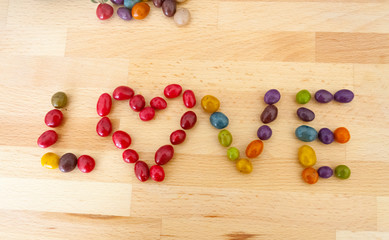 Naklejka na ściany i meble the word love which is laid out of multi-colored candies on a wooden board