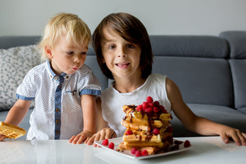 Sweet toddler birthday boy and his brothers, eating belgian waffle with raspberries and chocolate for breakfast