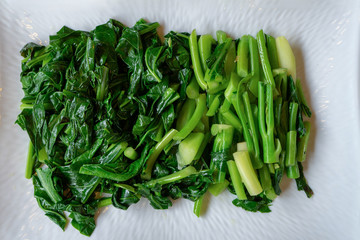 Seperate slided and boiled Chinese (Thai) KALE vegetable lay on the white rectangle on the wood...