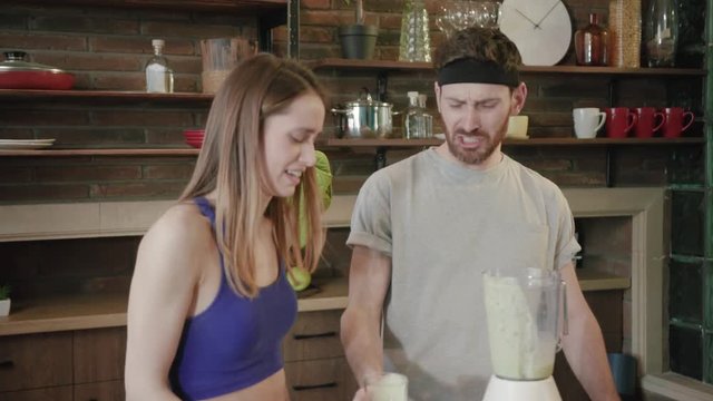 Young fitness couple tasting green smoothie are disgusted with its taste in kitchen at home. Facial expression, emotional, negative mood. Healthy food, tasteless, tastes bad. Close up view