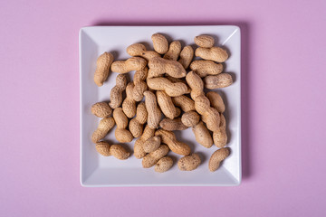Peanuts in white square shaped plate minimal on purple background backdrop food nut texture copy space top view