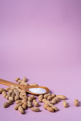 Peanuts and wooden spatula with salt minimal on purple background backdrop food nut texture copy space angle view