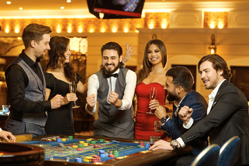 Group happy people make bets gambiling at the roulette table in the casino.